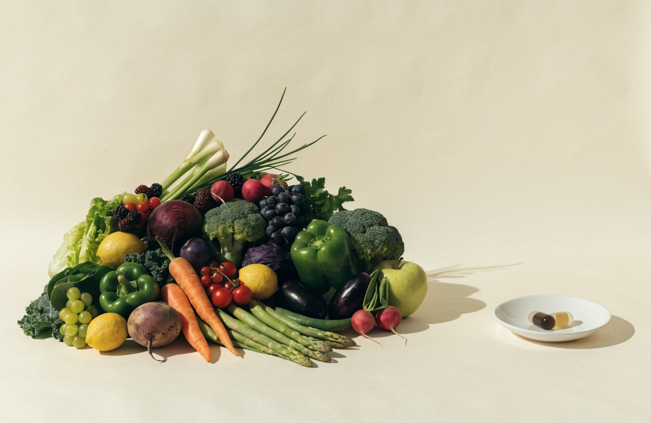 An abundant spread of fresh fruit and vegetables beside a small dish holding two capsules